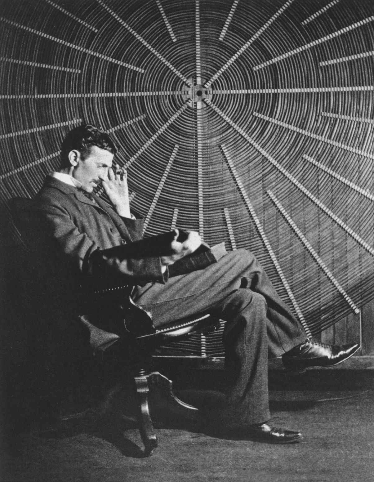 Tesla sedící před spirálovou cívkou používanou při experimentech s bezdrátovým napájením v jeho laboratoři East Houston St