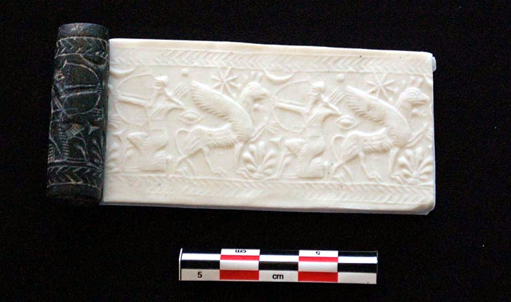 Bu silindir mühür yaklaşık 2,600 yıl öncesine, Asurluların Idu'yu yeniden fethetmesinden sonraki bir zamana kadar uzanıyor. Aslen bir saraydan gelmiş olabilecek mühür, bir parça kil üzerine yuvarlanırsa (burada bu resimde yeniden inşa edilmiştir) efsanevi bir sahne gösterecektir. Tanrı Ninurta olabilecek çömelmiş bir okçuyu bir grifona dönük olarak betimler. Bir ay hilali (ay tanrısını temsil eder), sekiz köşeli bir sabah yıldızı (tanrıça İştar'ı temsil eder) ve bir palmet kolayca görülür. © Resim kredisi: Cinzia Pappi'nin izniyle
