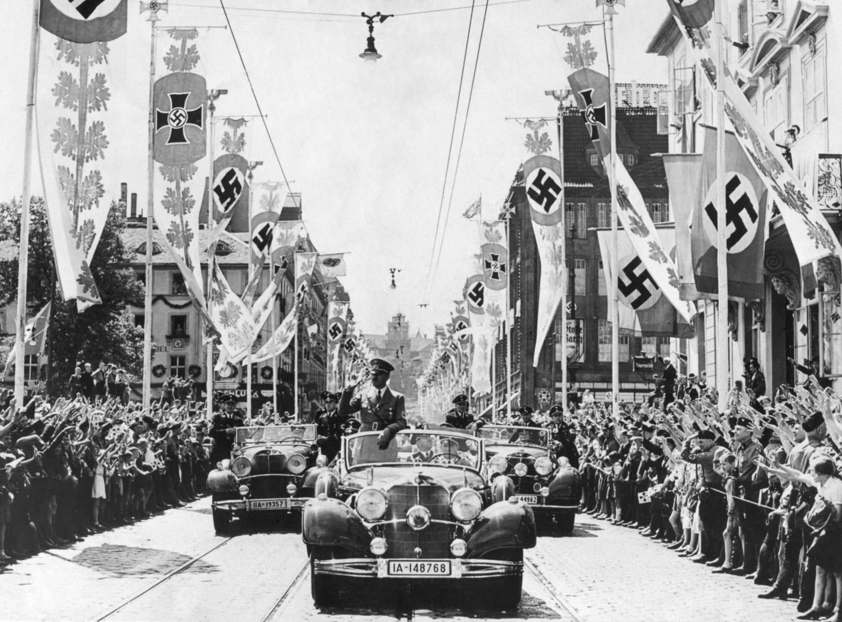 Ādolfs Hitlers parādes priekšgalā pamāja pūļiem no savas automašīnas. Ielas rotā dažādi svastikas baneri. Ca. 1934-38. Hitleram bija ērts, bet neīsts iemesls, kāpēc par zīmotni izvēlējās svastikas simbolu. Otrajā tūkstošgadē to izmantoja Indijas āriešu nomadi. Nacistu teorijā āriešiem bija vācu senči, un Hitlers secināja, ka svastika ir bijusi mūžīgi antisemītiska.