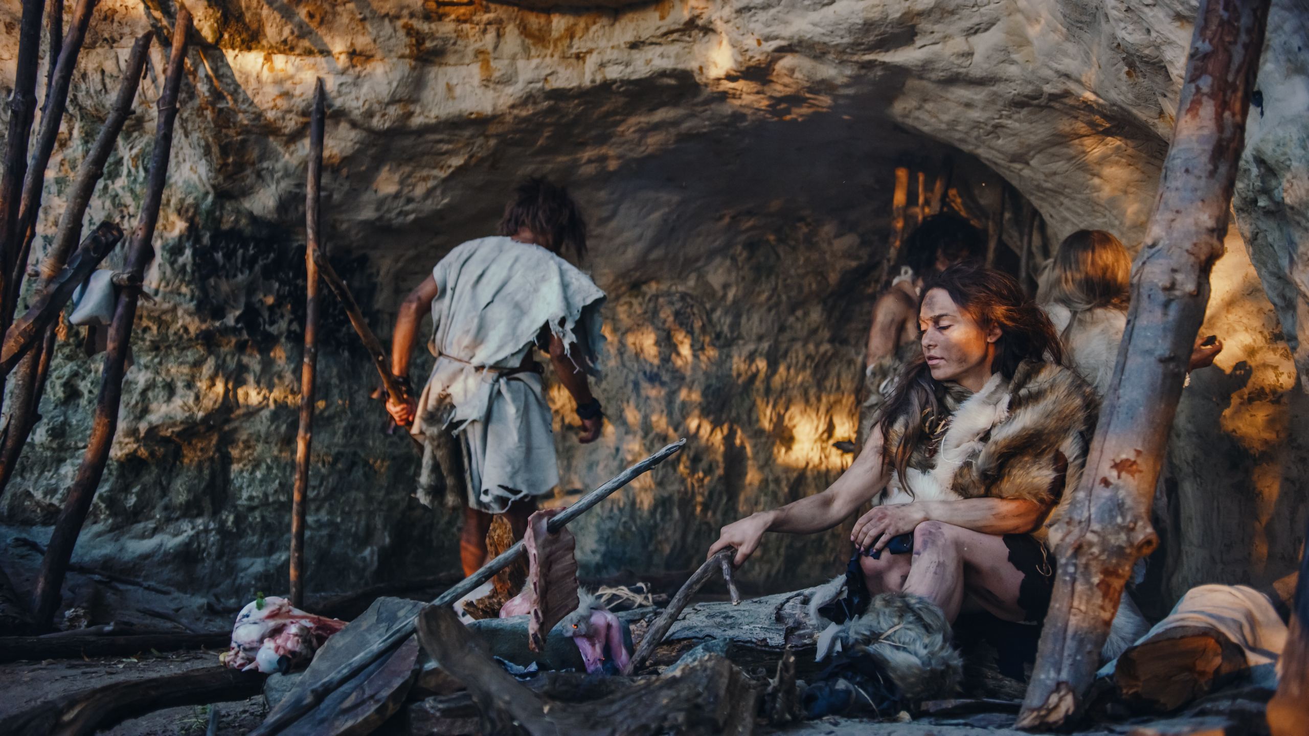Gambar rekreasi Keluarga Homo Sapiens Neanderthal. Suku Pemburu-Pengumpul Mengenakan Kulit Binatang Tinggal di Gua. Pemimpin Membawa Hewan Mangsa dari Perburuan, Wanita Memasak Makanan di Api Unggun, Gadis Menggambar di Wals Menciptakan Seni.